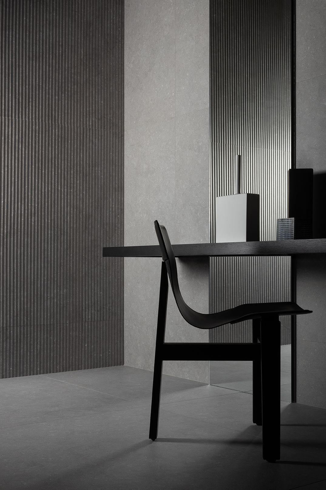 Silla minimalista negra junto a una mesa en un interior moderno gris con paneles de pared a rayas.