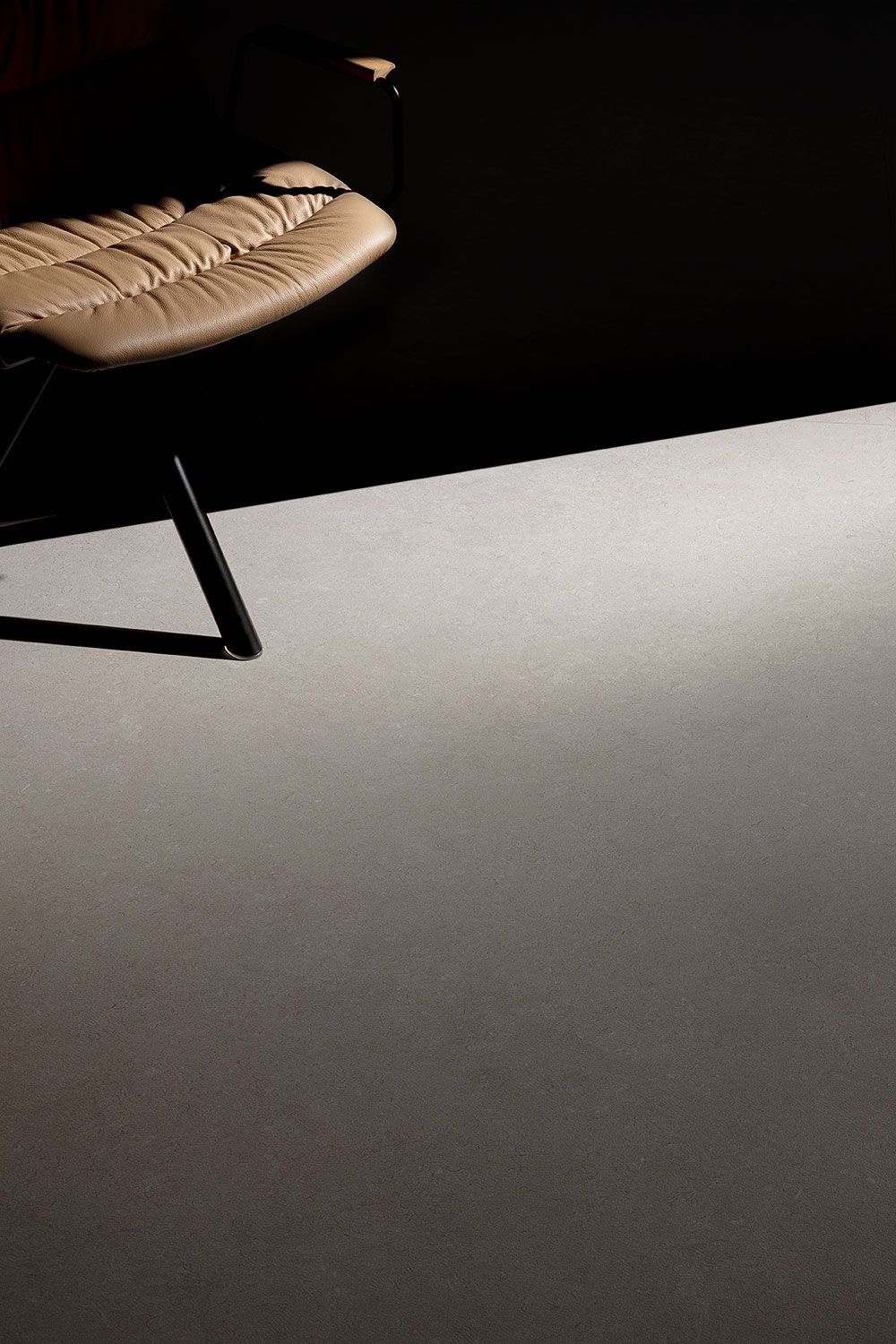 Silla de mimbre iluminada por un foco sobre un suelo y una pared oscuros.