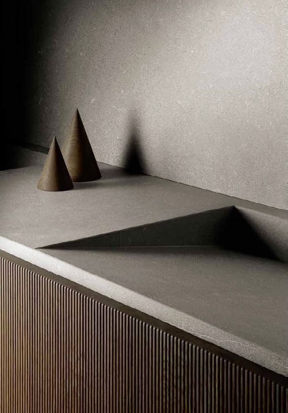 Tablero minimalista gris con tres conos y una marcada sombra triangular sobre una pared texturizada.
