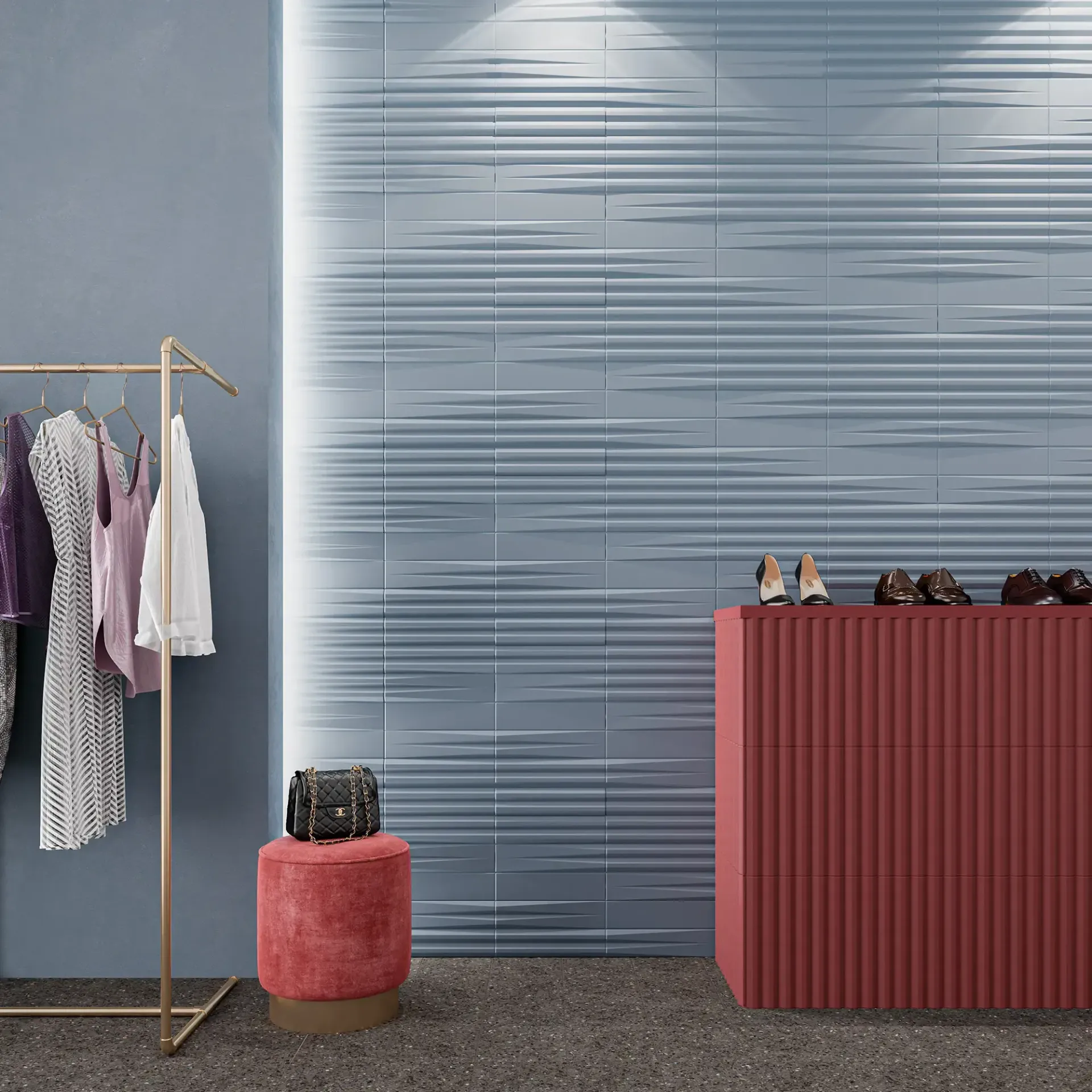 Exhibición minimalista de ropa con prendas colgadas, un pequeño taburete y un mostrador rojo sobre una pared azul texturizada.