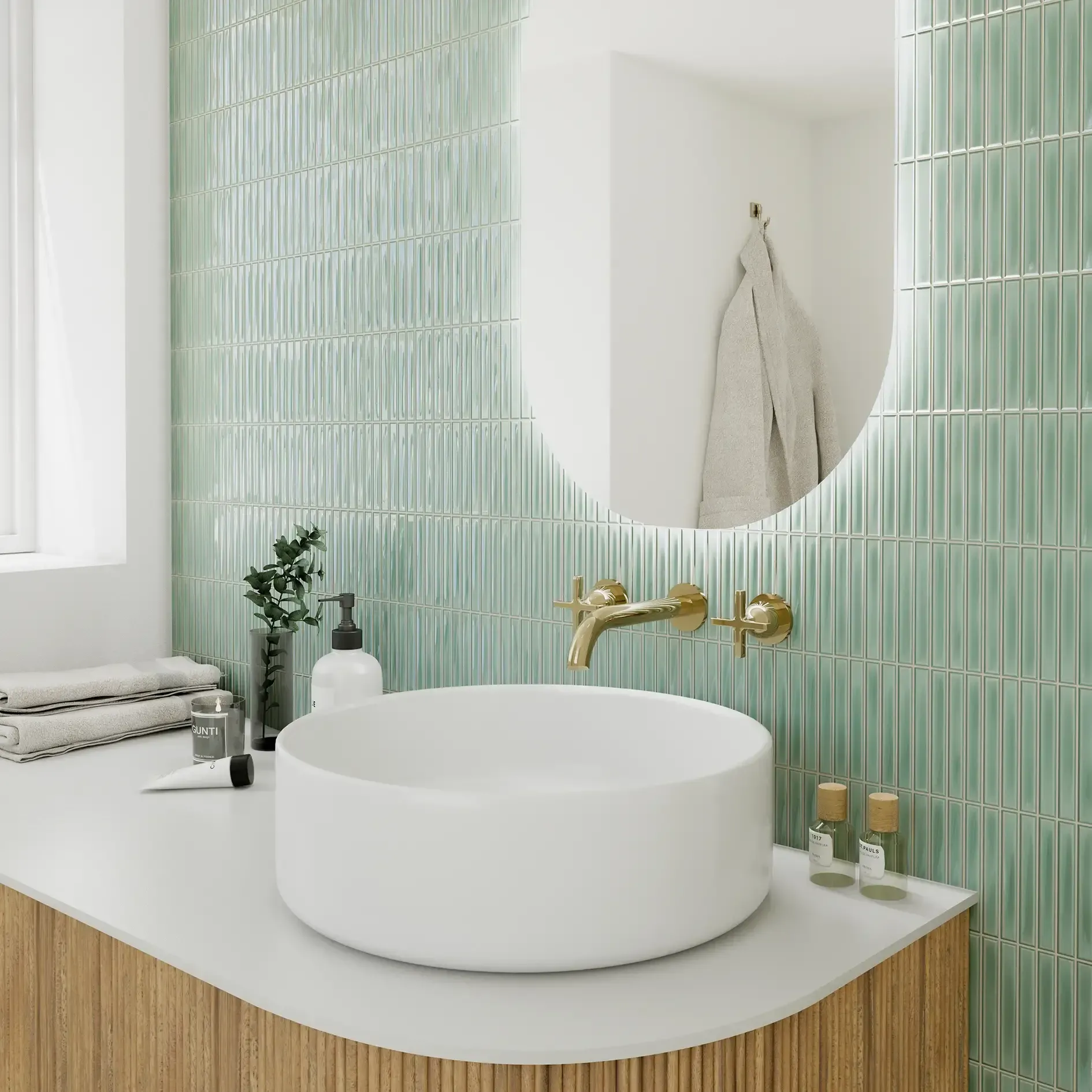 Lavabo moderno con espejo redondo, grifo de latón, pared alicatada en verde menta y tocador de madera.