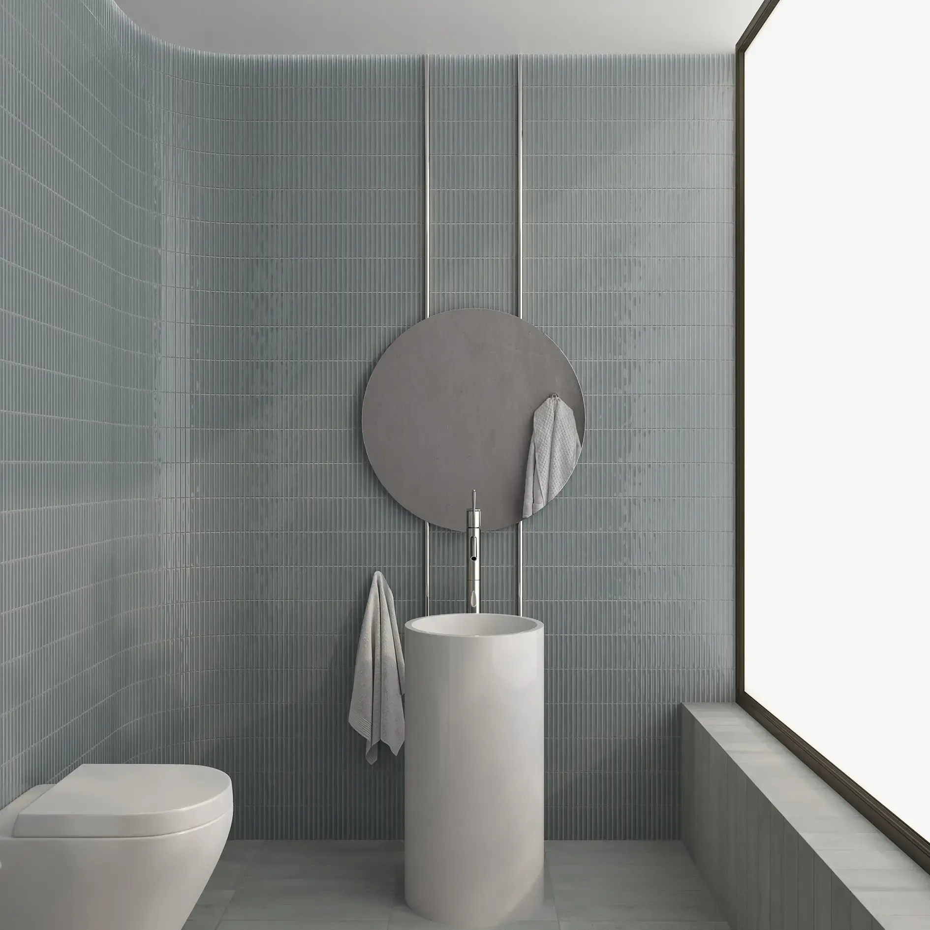 Baño minimalista con pared de azulejos grises, espejo redondo, lavabo con pedestal e inodoro.