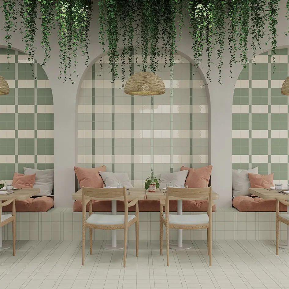 Interior acogedor de cafetería en tonos pastel con lámparas colgantes de mimbre, pared a cuadros, asientos rosas y mesas de madera.