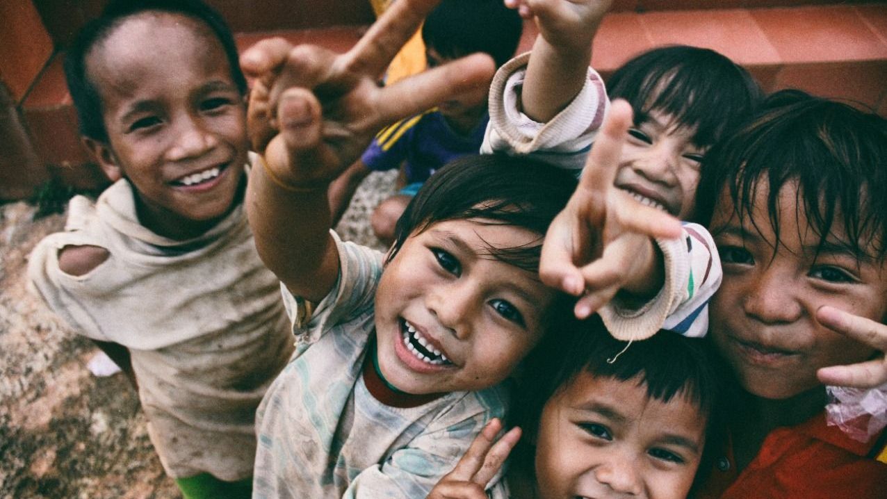 A group of children are giving peace signs and smiling for the camera.