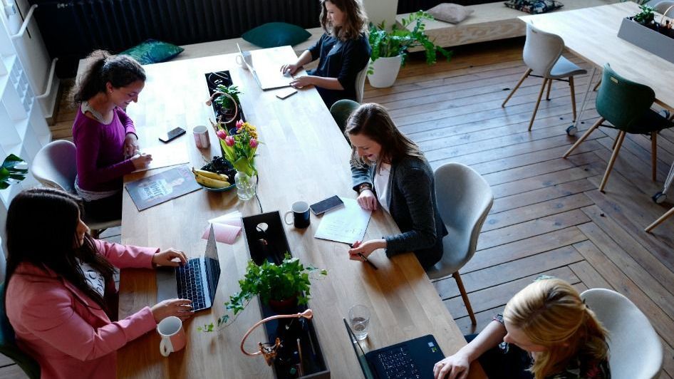 A group of women are sitting around a table with laptops.
