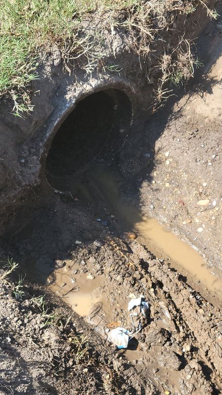 A muddy hole in the ground with a pipe coming out of it.