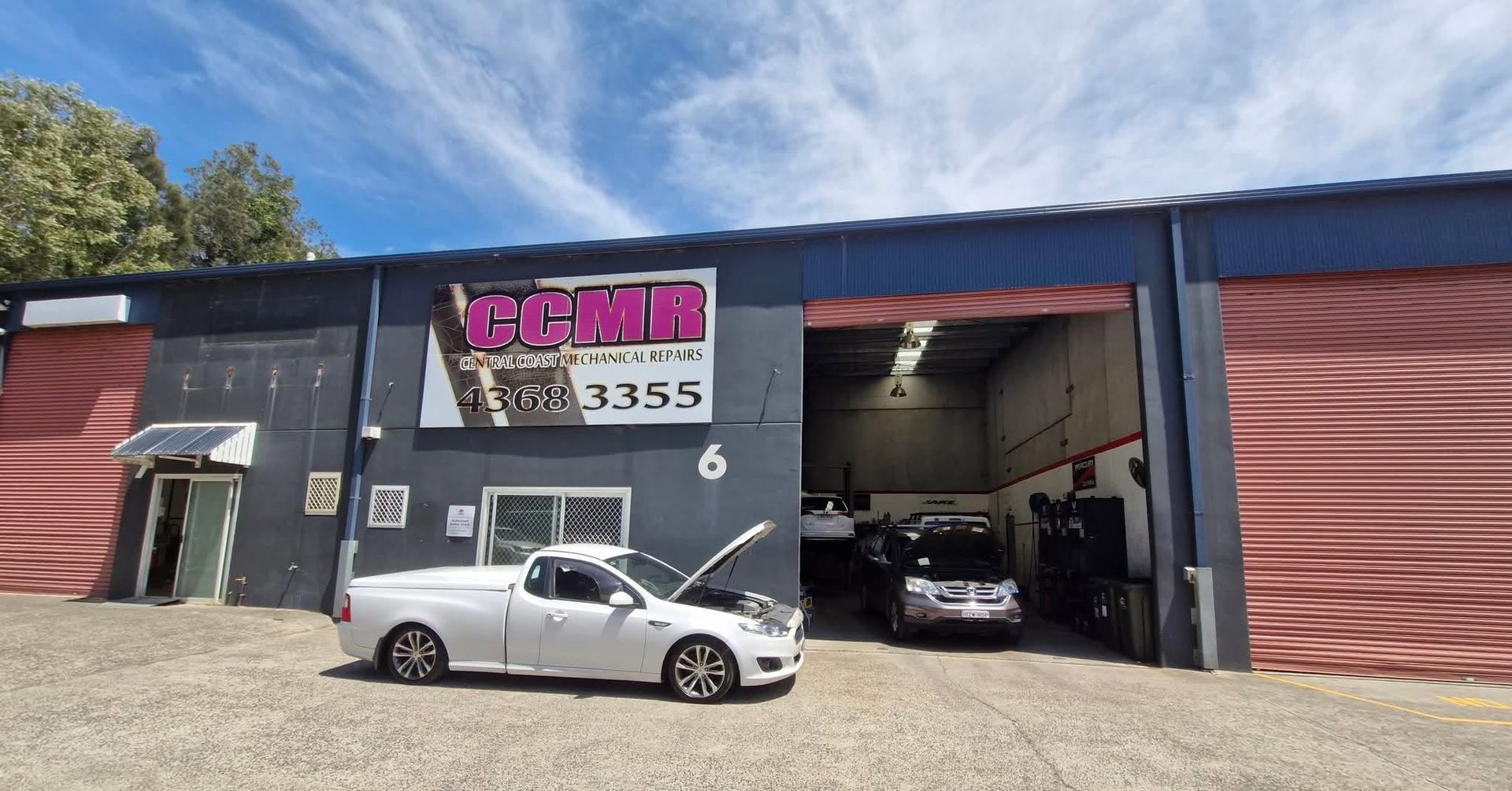 Car shop exterior with open garage bays and two parked cars, one white convertible in front