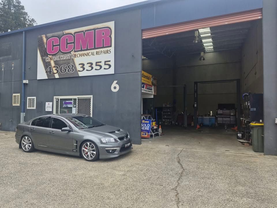 Auto repair shop exterior with an open garage bay and a gray car parked outside