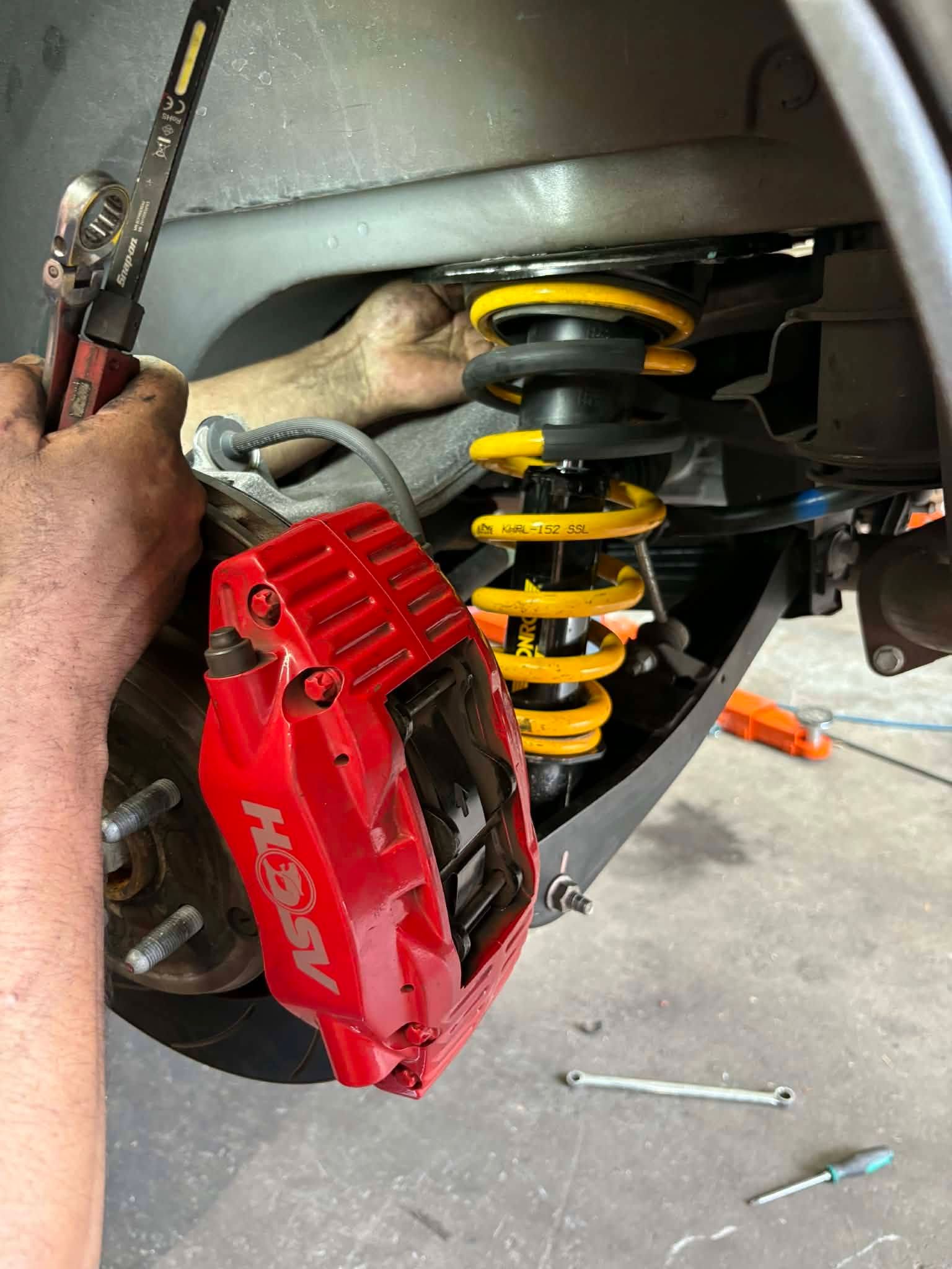 Red brake caliper beside a yellow suspension spring on a car during repair
