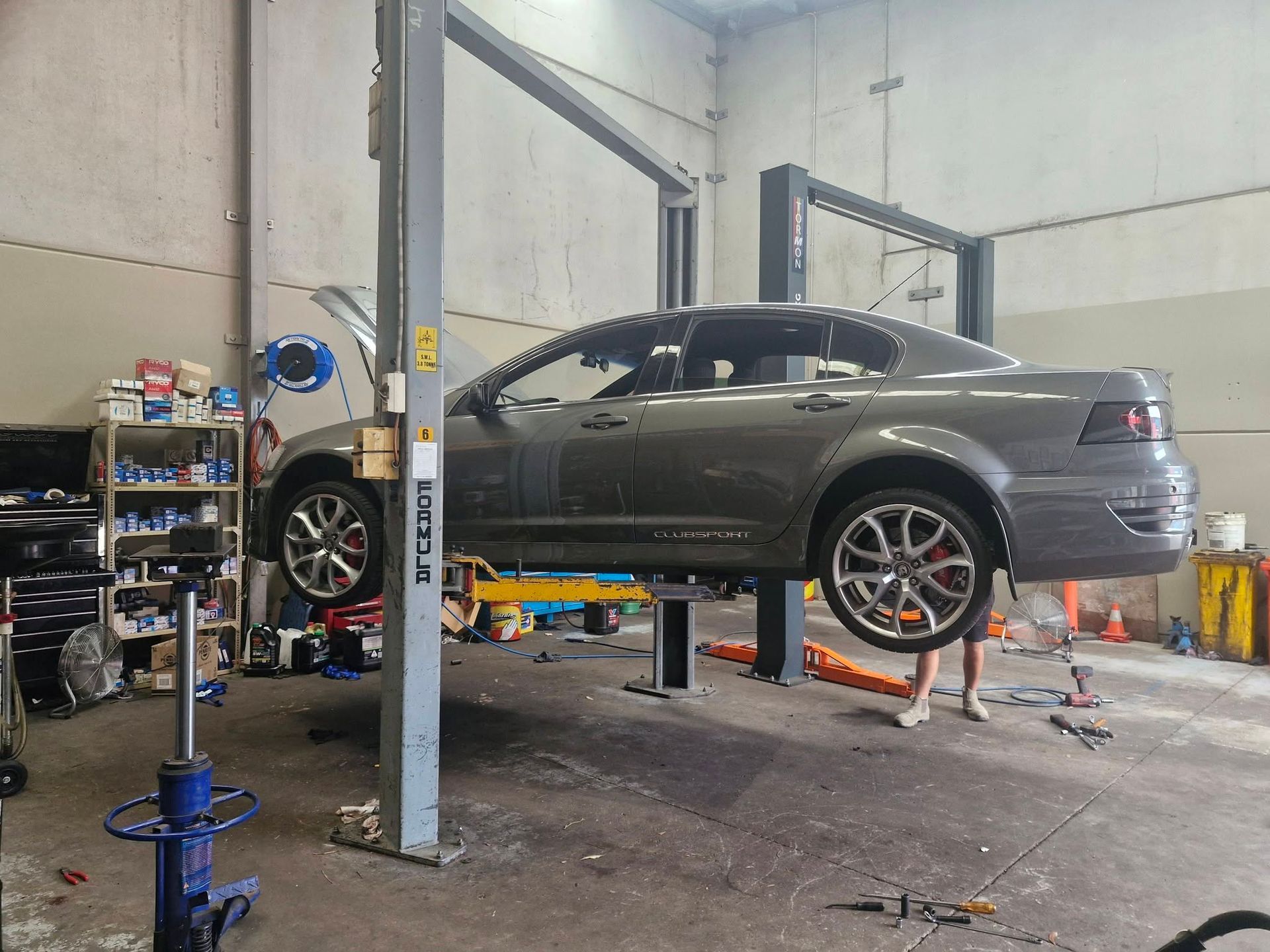 Gray sedan on a hydraulic lift in an auto repair shop, with tools and equipment nearby.