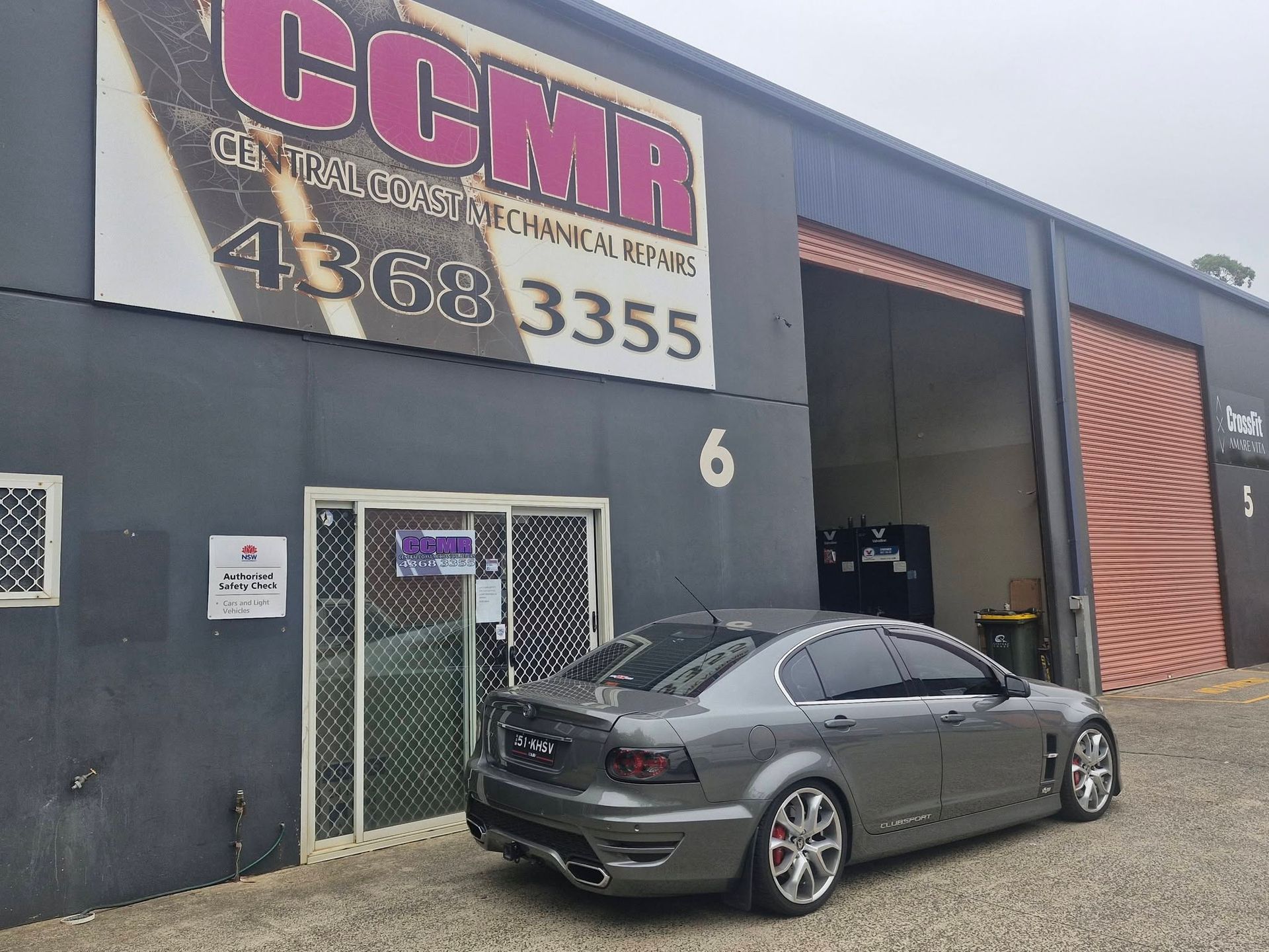 Gray sedan parked outside CCMR auto shop with open garage door and sign above entrance