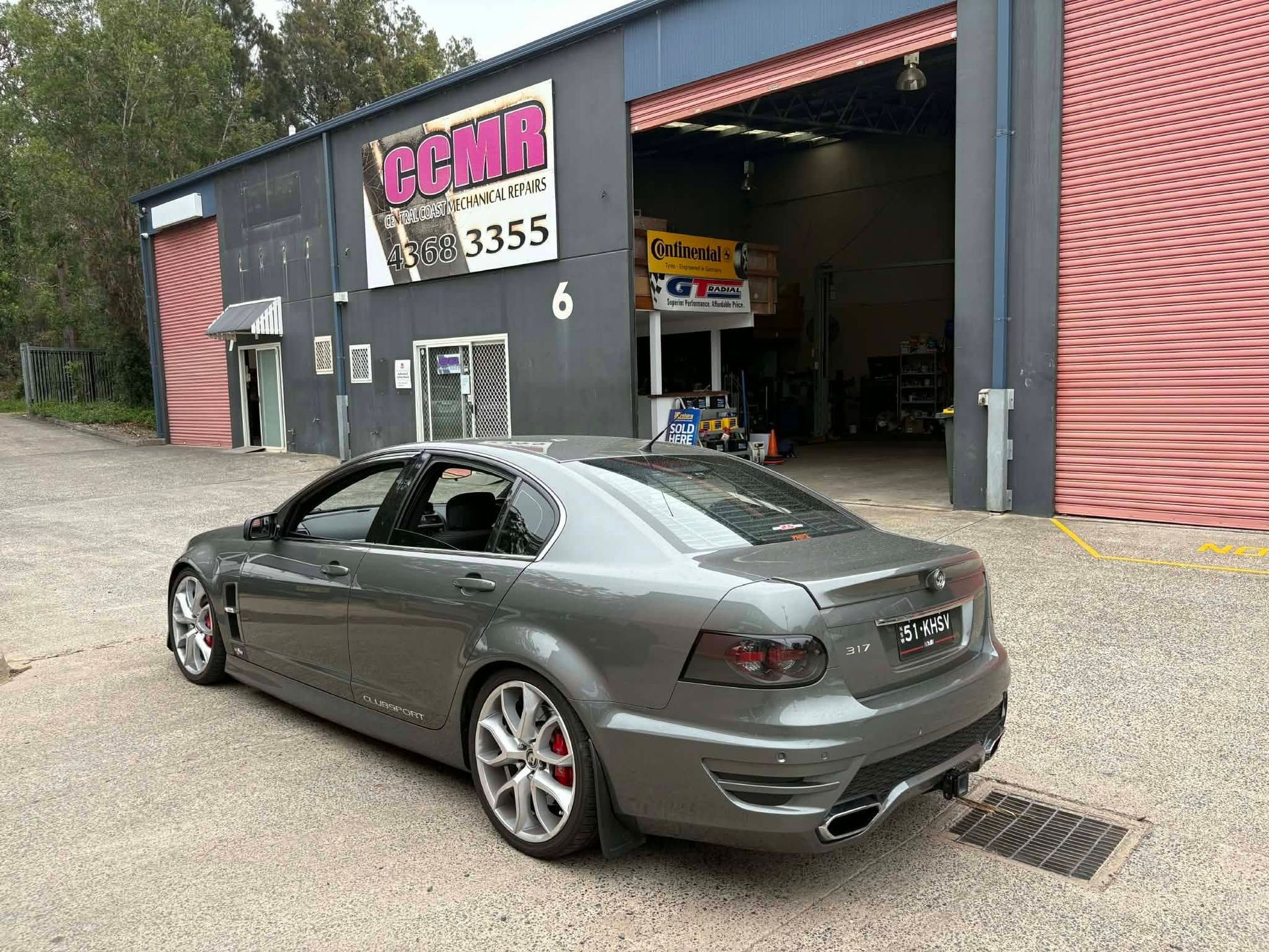 Silver sedan parked outside a garage with a pink sign and open service bay.