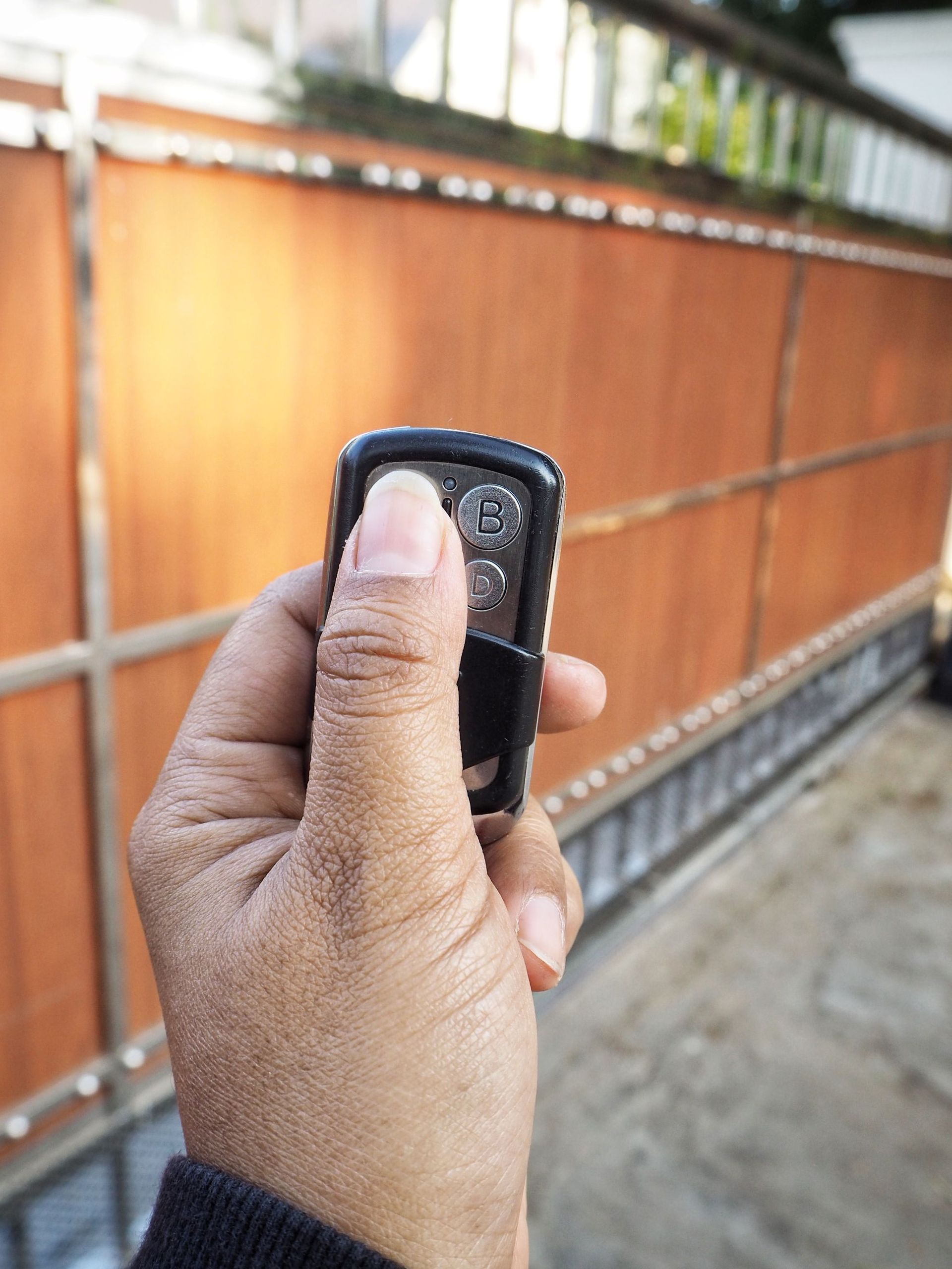 Hand holding a black remote in front of an orange wooden fence outdoors