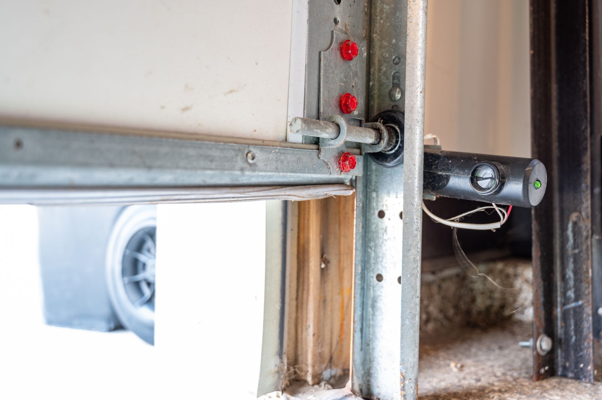 Garage door track with a mounted black sensor and a visible car outside through the opening