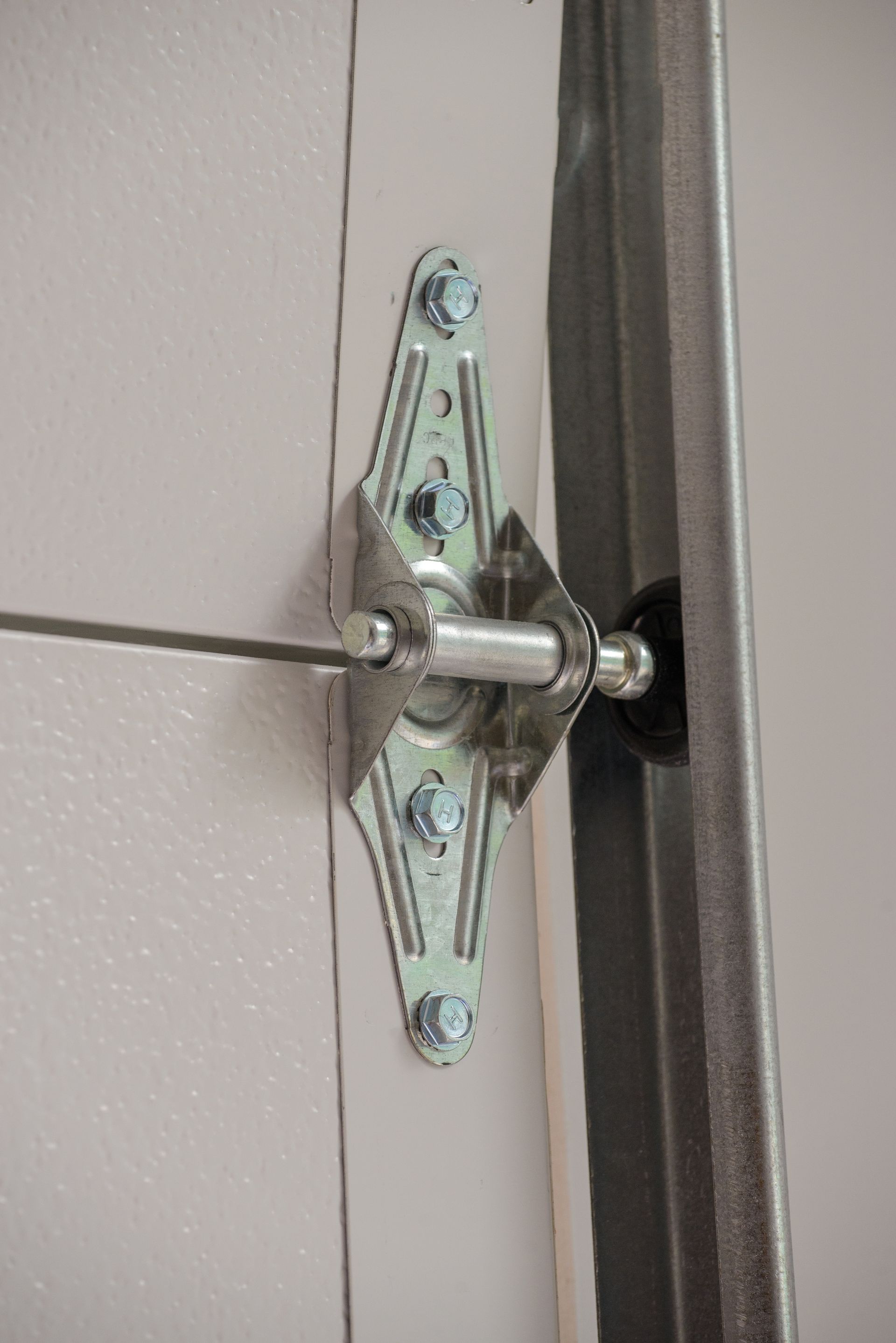 Close-up of a metal garage door hinge and roller attached to a gray panel.
