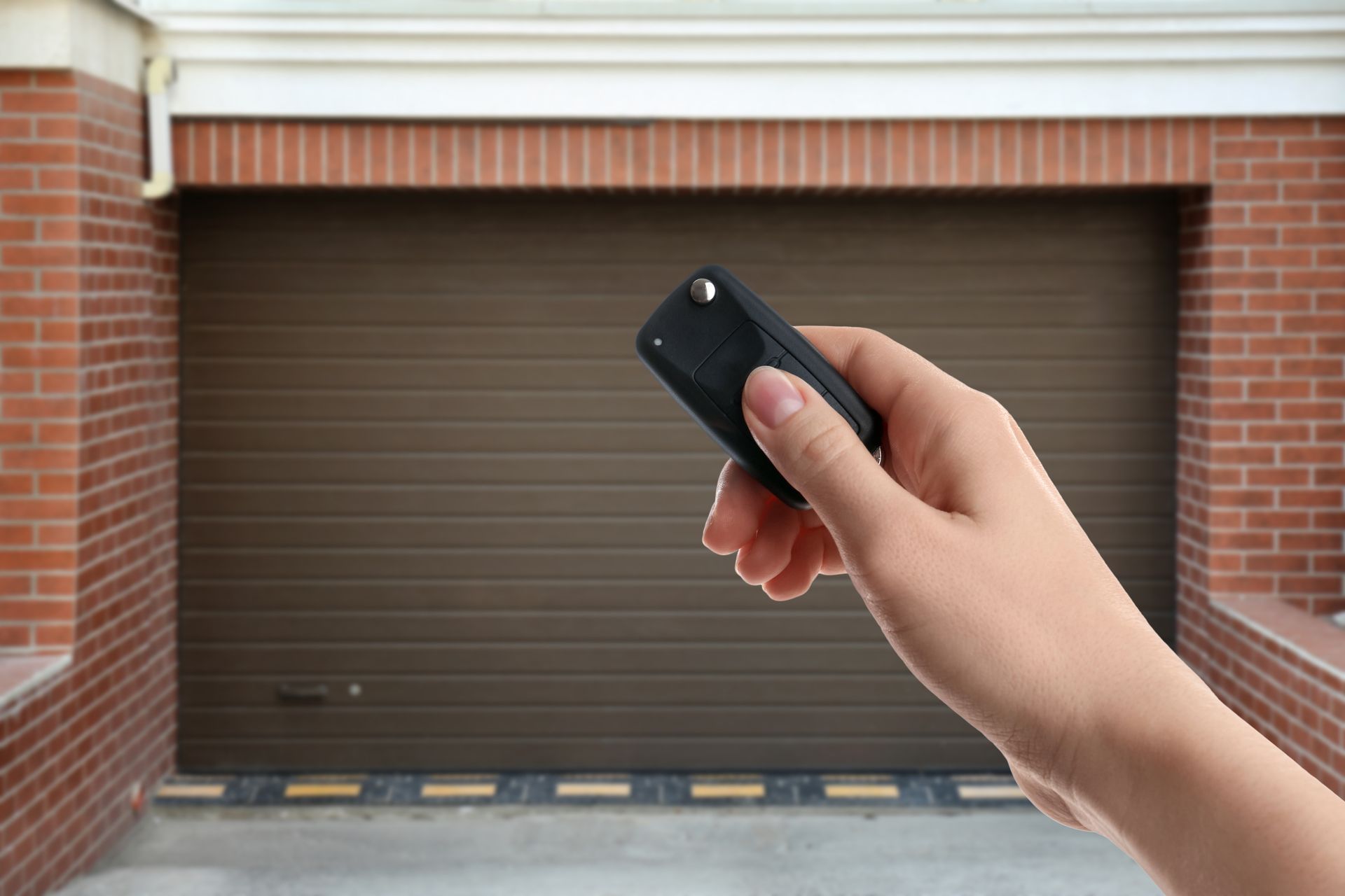 Hand holding a garage remote aimed at a closed brown garage door