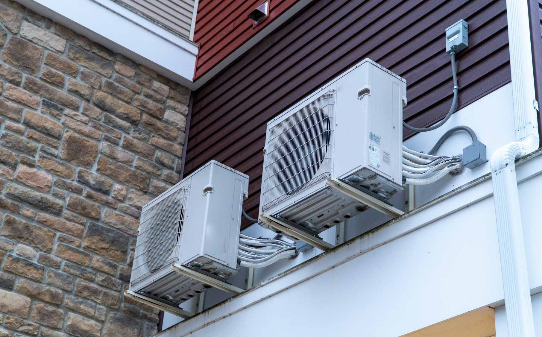Two wall-mounted outdoor air conditioner units on a building exterior above a white awning.