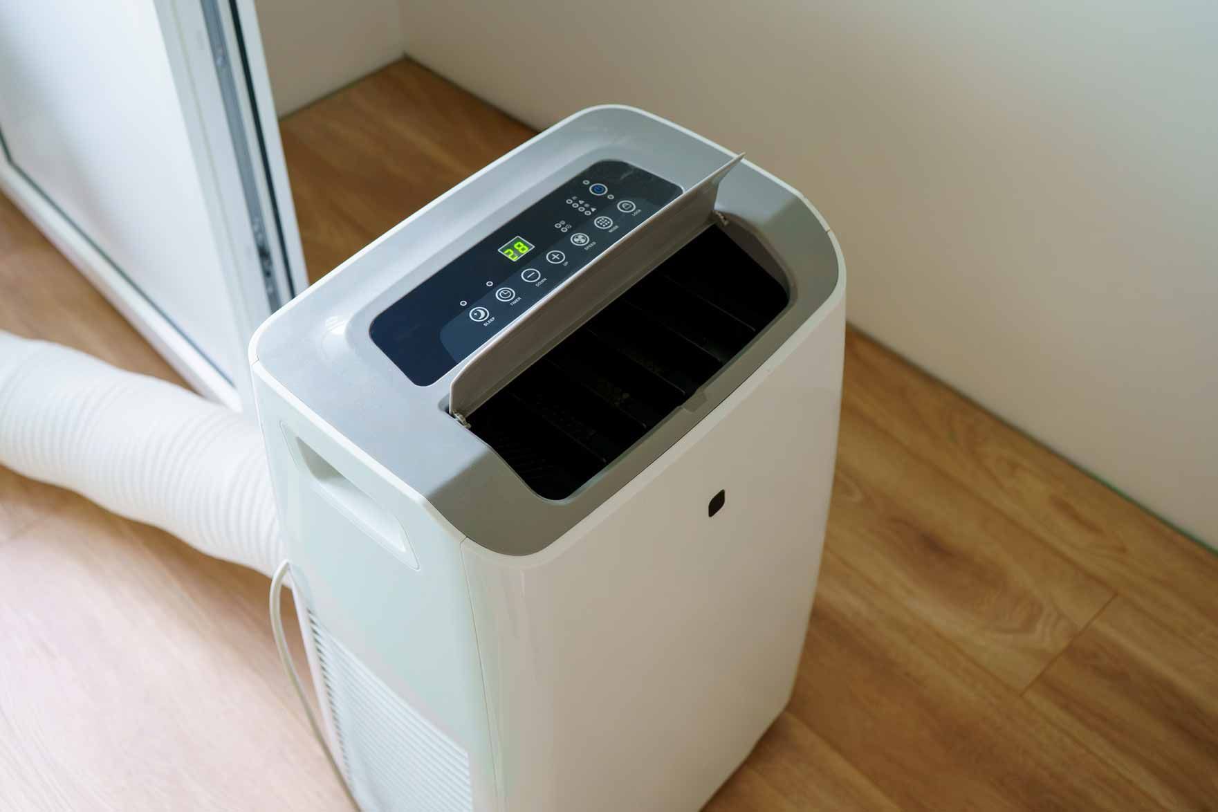 Portable air conditioner with a top control panel and flexible exhaust hose in a room corner