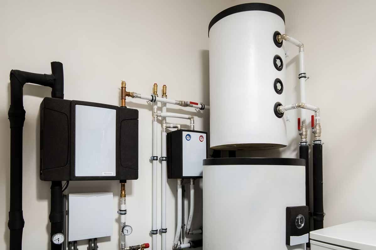 Industrial water heater and piping system in a utility room, with large white tanks and black mounted units.