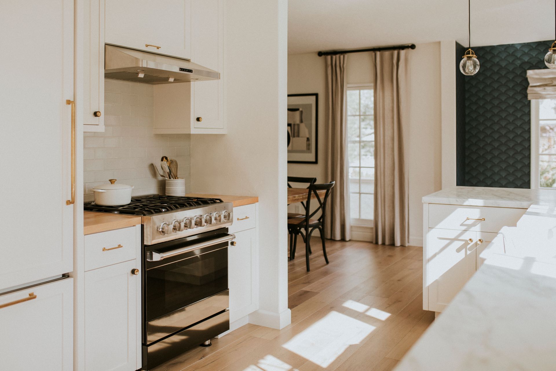 Bright modern kitchen with white cabinets, stove, island, and sunlight through nearby curtains