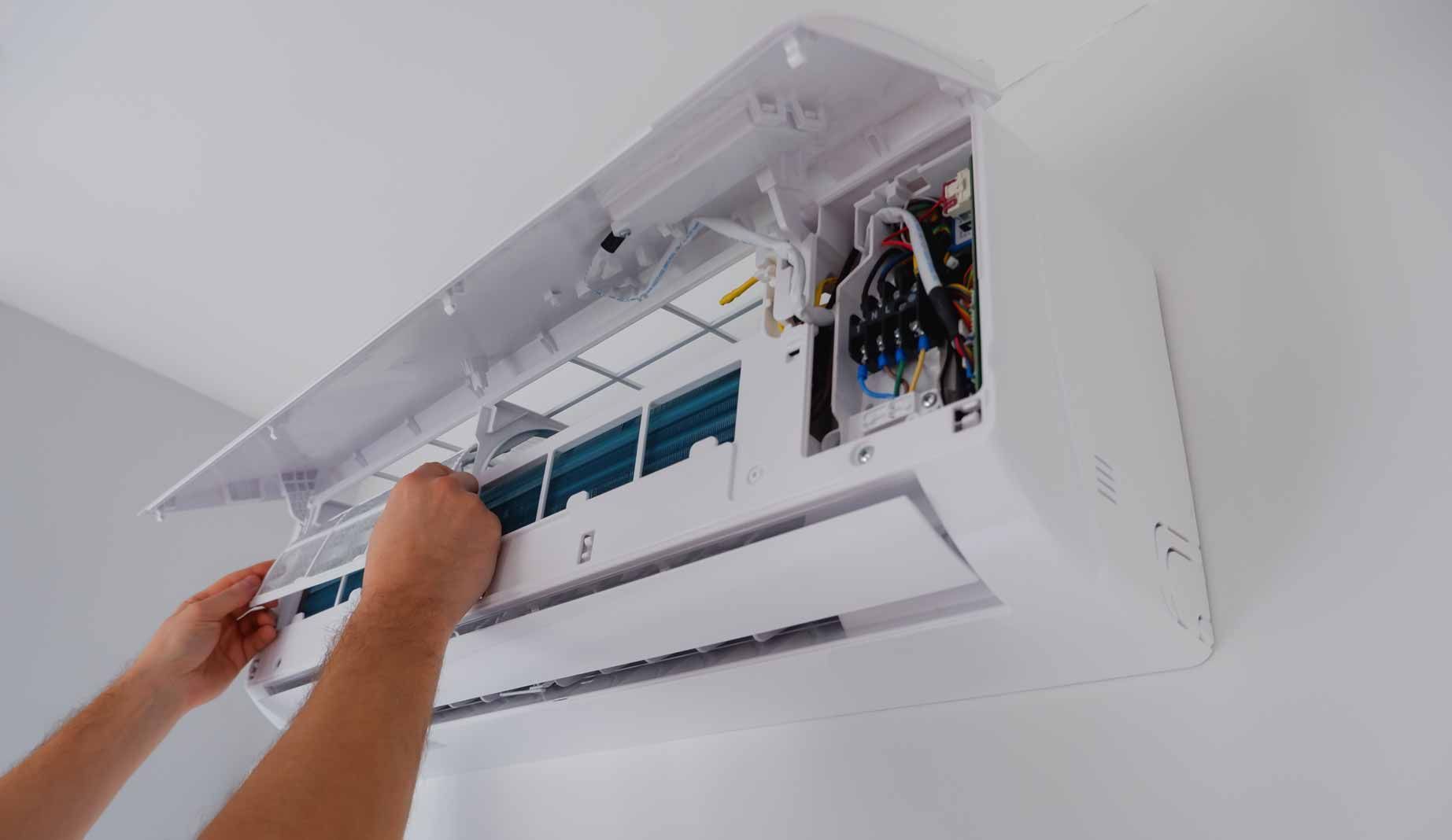 Technician cleaning the interior of a wall-mounted air conditioner with the cover open