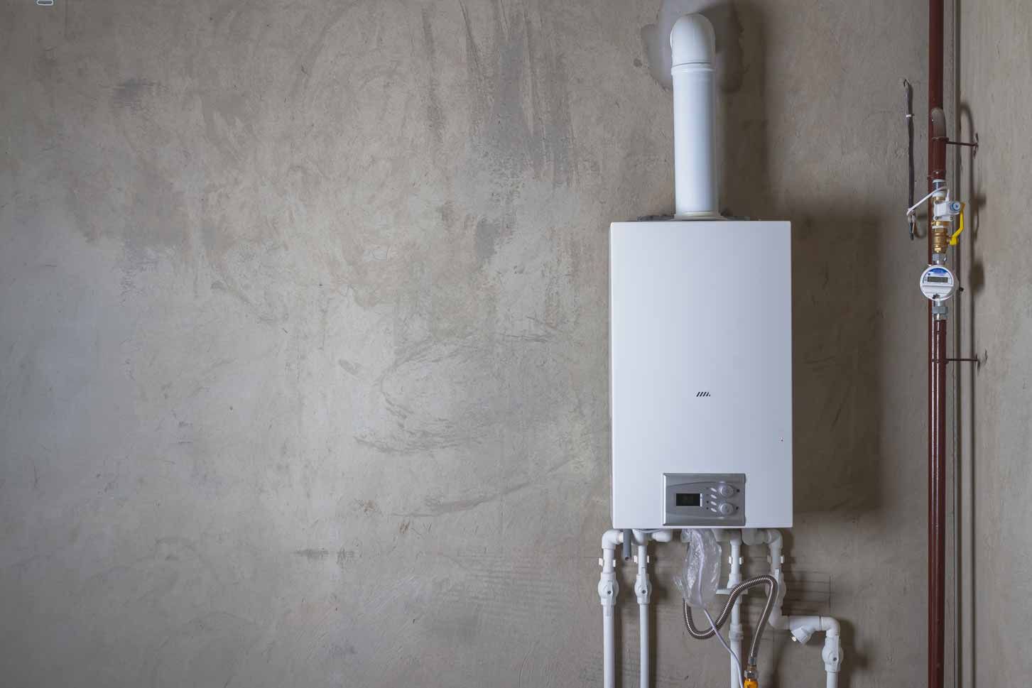 White wall-mounted boiler with exposed pipes against a concrete wall