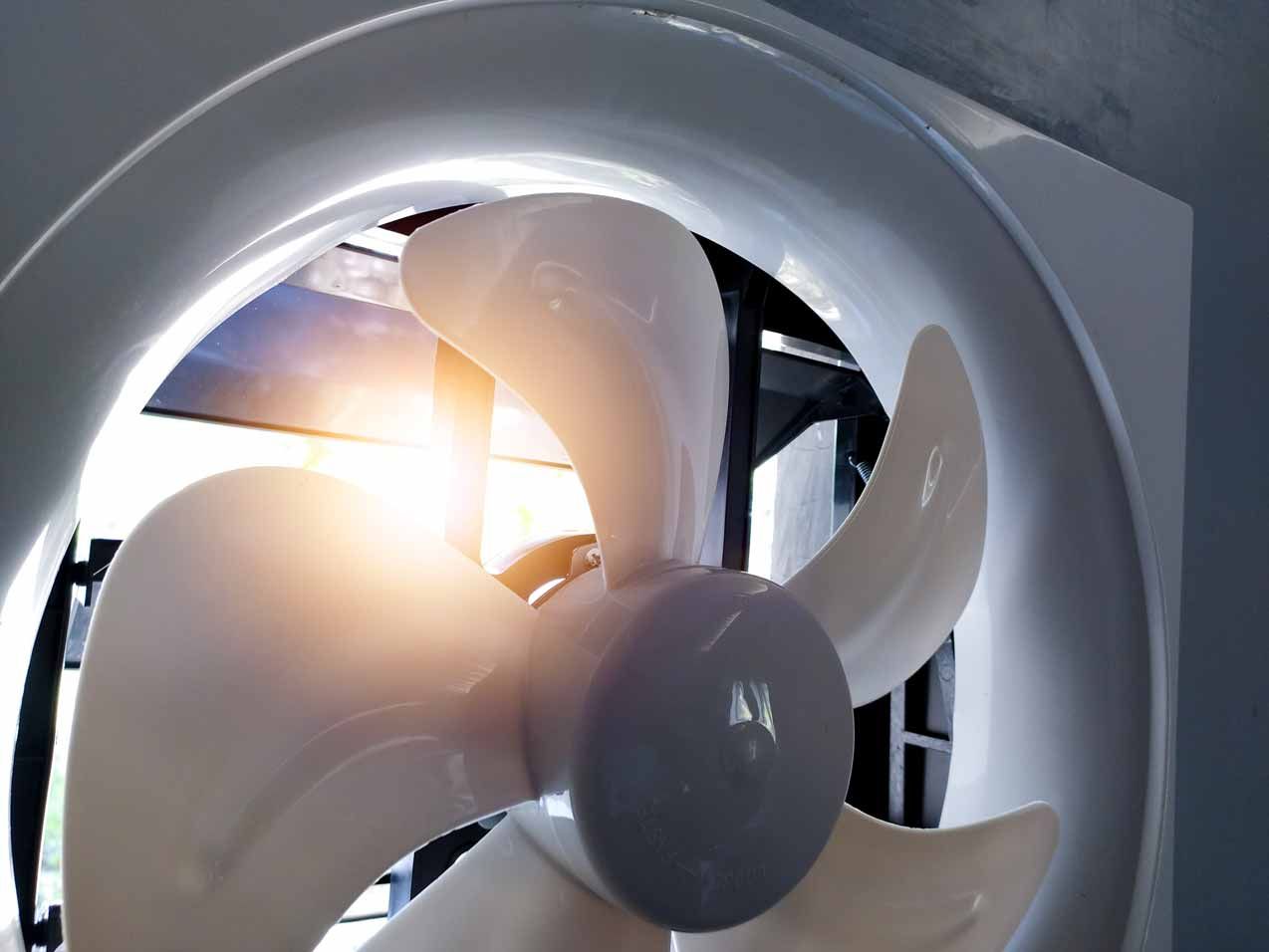 Close-up of a white ceiling fan with a gray center, lit by a bright lamp behind it.