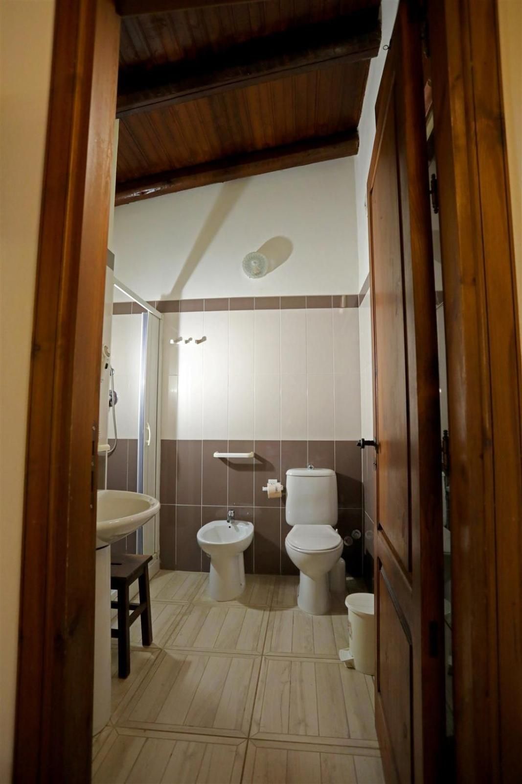 Piccolo bagno rustico con pavimento piastrellato, WC, bidet, lavabo e soffitto inclinato in legno.