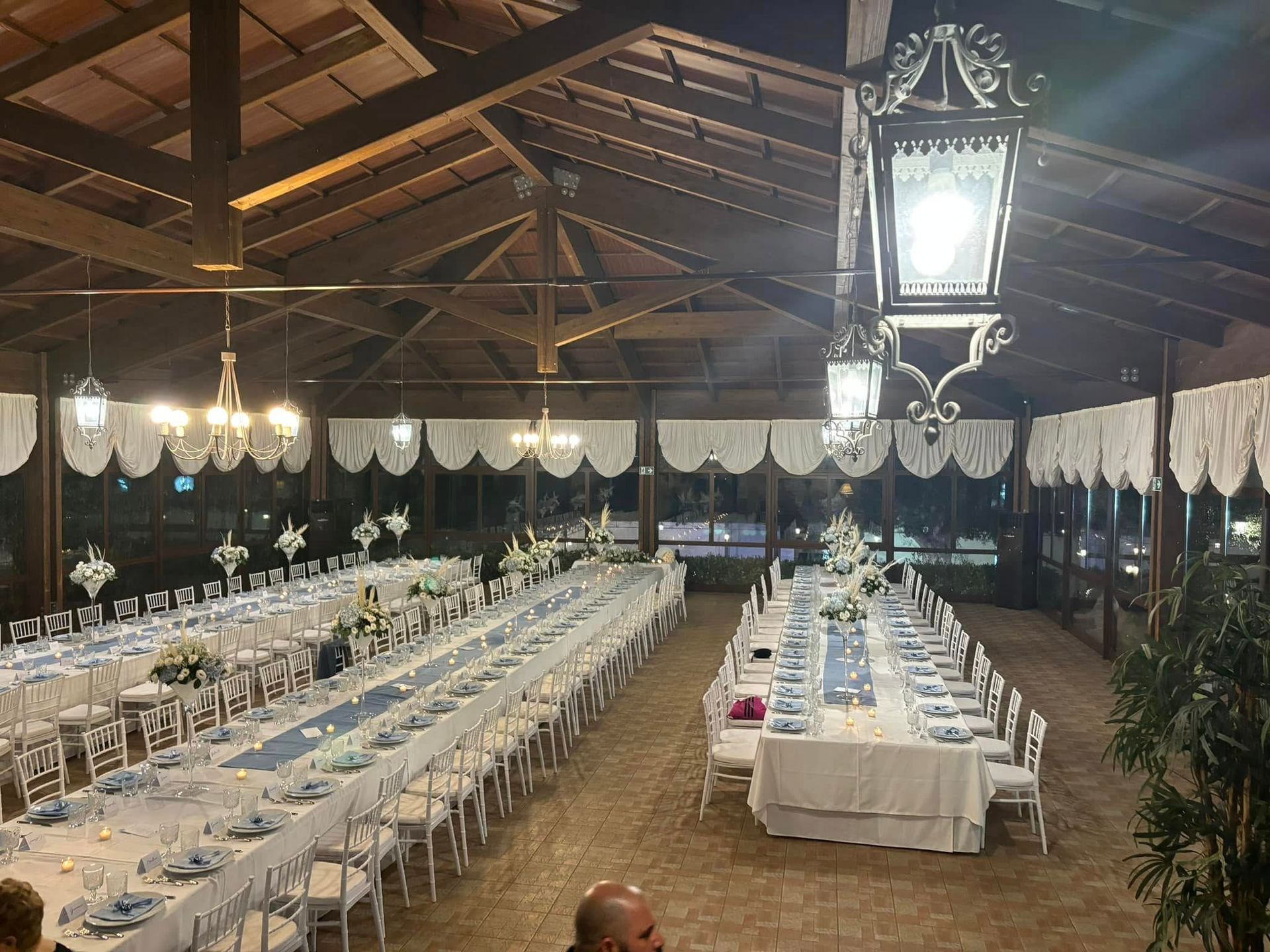 Lunga sala da banchetto con tovaglie bianche, lampadari e file di tavoli apparecchiati per un evento
