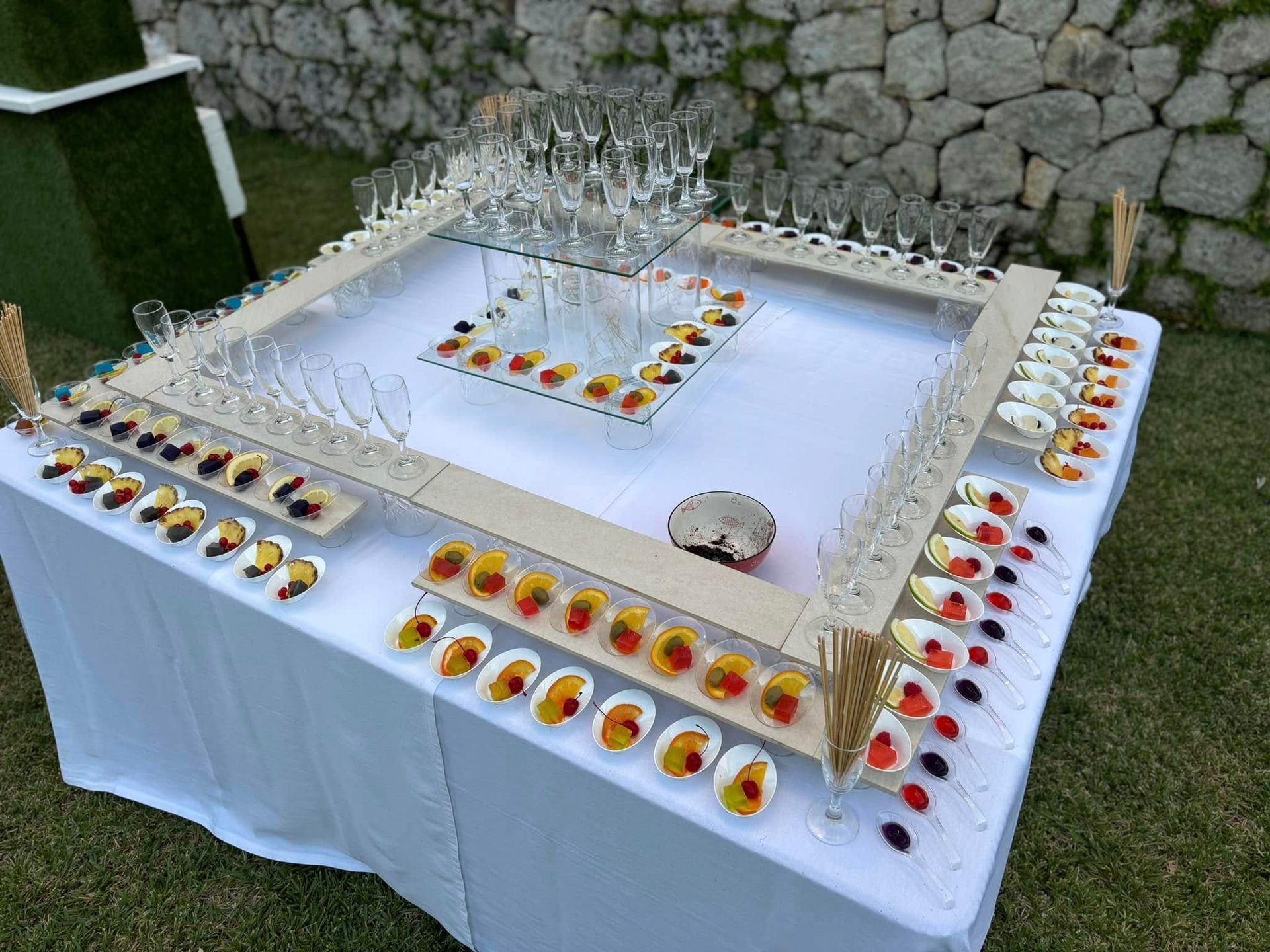 Commemorazione all'aperto con drappo bianco, candele, fiori e un elemento centrale in vetro simile a una fontana.