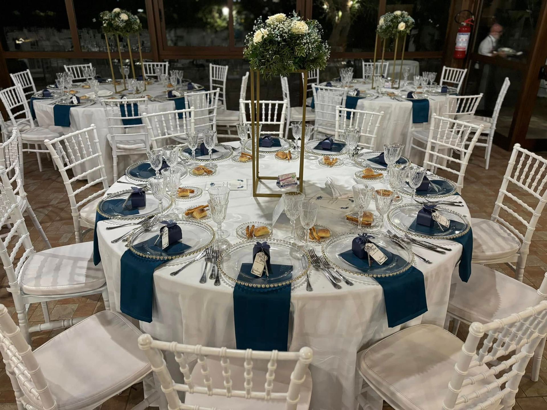 Sala per banchetti con tavoli rotondi ricoperti da drappeggi bianchi e sedie sotto un tetto di legno, allestita per un evento.