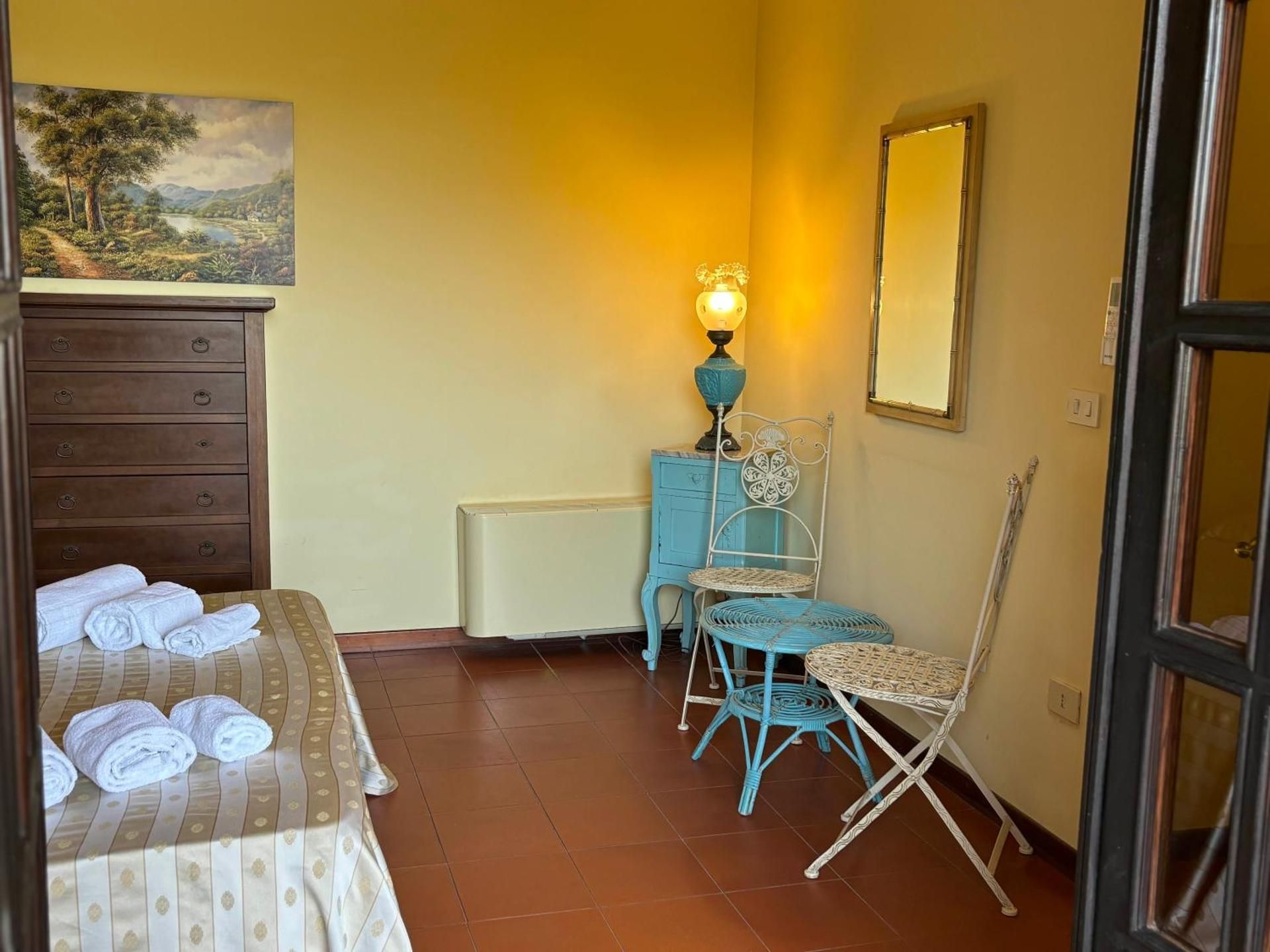 Piccola camera da letto con pareti gialle, letto singolo, comò, lampada blu, specchio e sedia turchese in un angolo.
