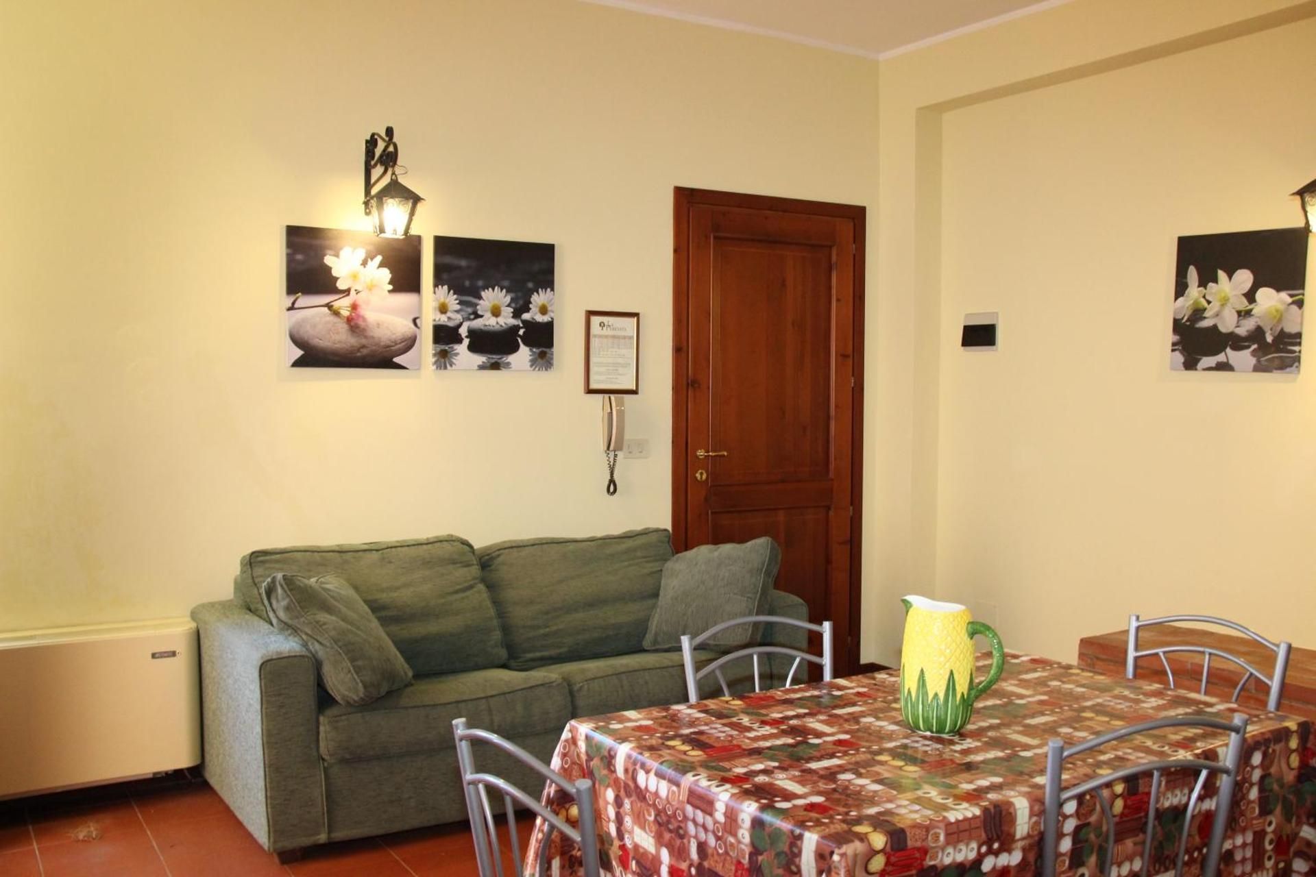 Soggiorno con divano verde, tavolo da pranzo, quadri alle pareti e porta in legno.