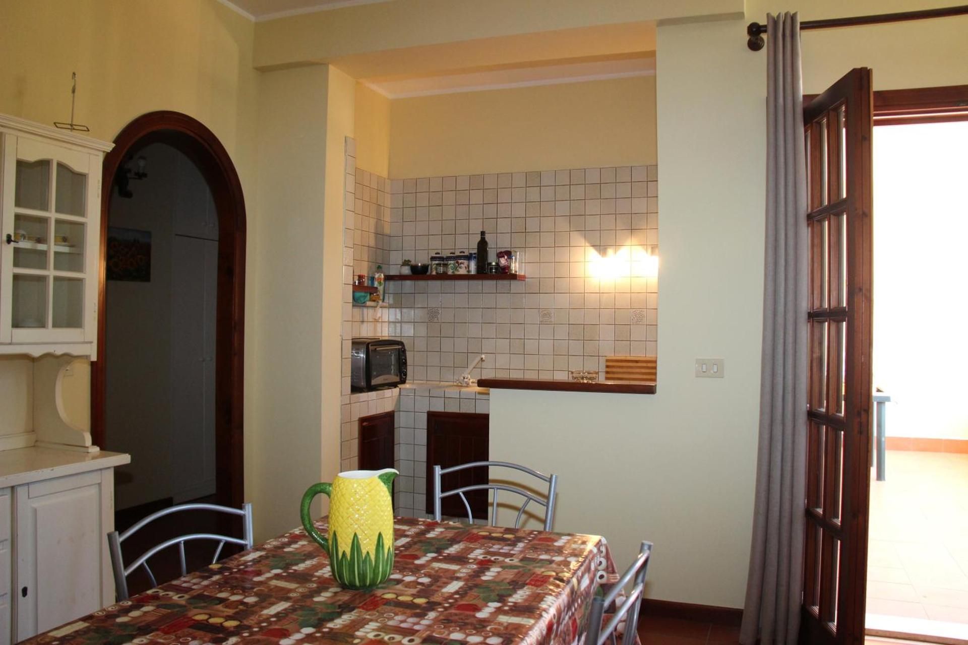 Sala da pranzo con tovaglia a fantasia, sedie e cucina a vista passavivande in luce calda