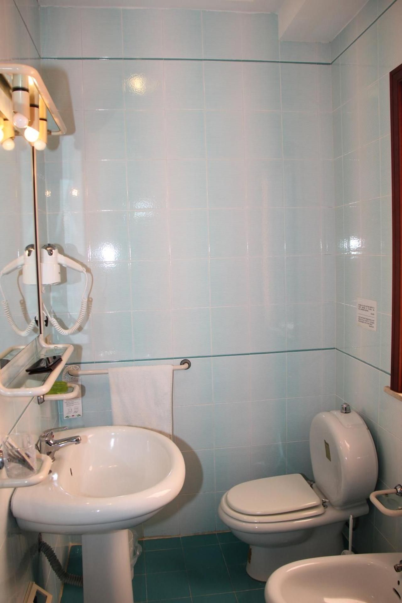 Piccolo bagno piastrellato con lavandino, WC, doccia e specchio con luce calda.