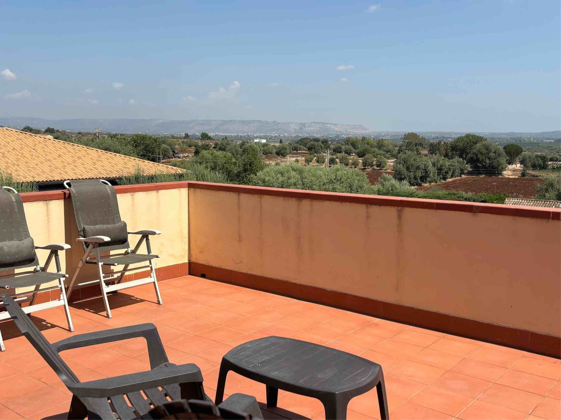 Terrazza con sedie e tavolo neri con vista su un paesaggio soleggiato e sulle colline in lontananza.