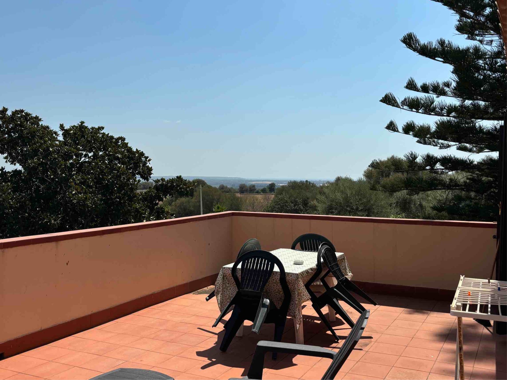Terrazza sul tetto con sedie e tavolo neri, affacciata sugli alberi sotto un cielo azzurro limpido.