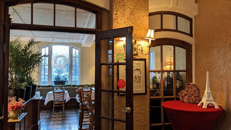Cozy restaurant entrance with open doors, lit wall sconces, and a red table holding a small Eiffel Tower decor.