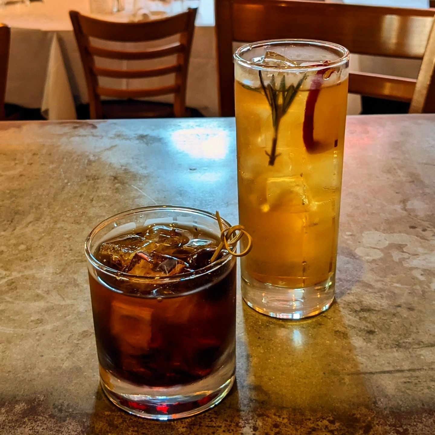 Two drinks on a table: a dark iced soda and a tall amber iced tea with lemon slices.