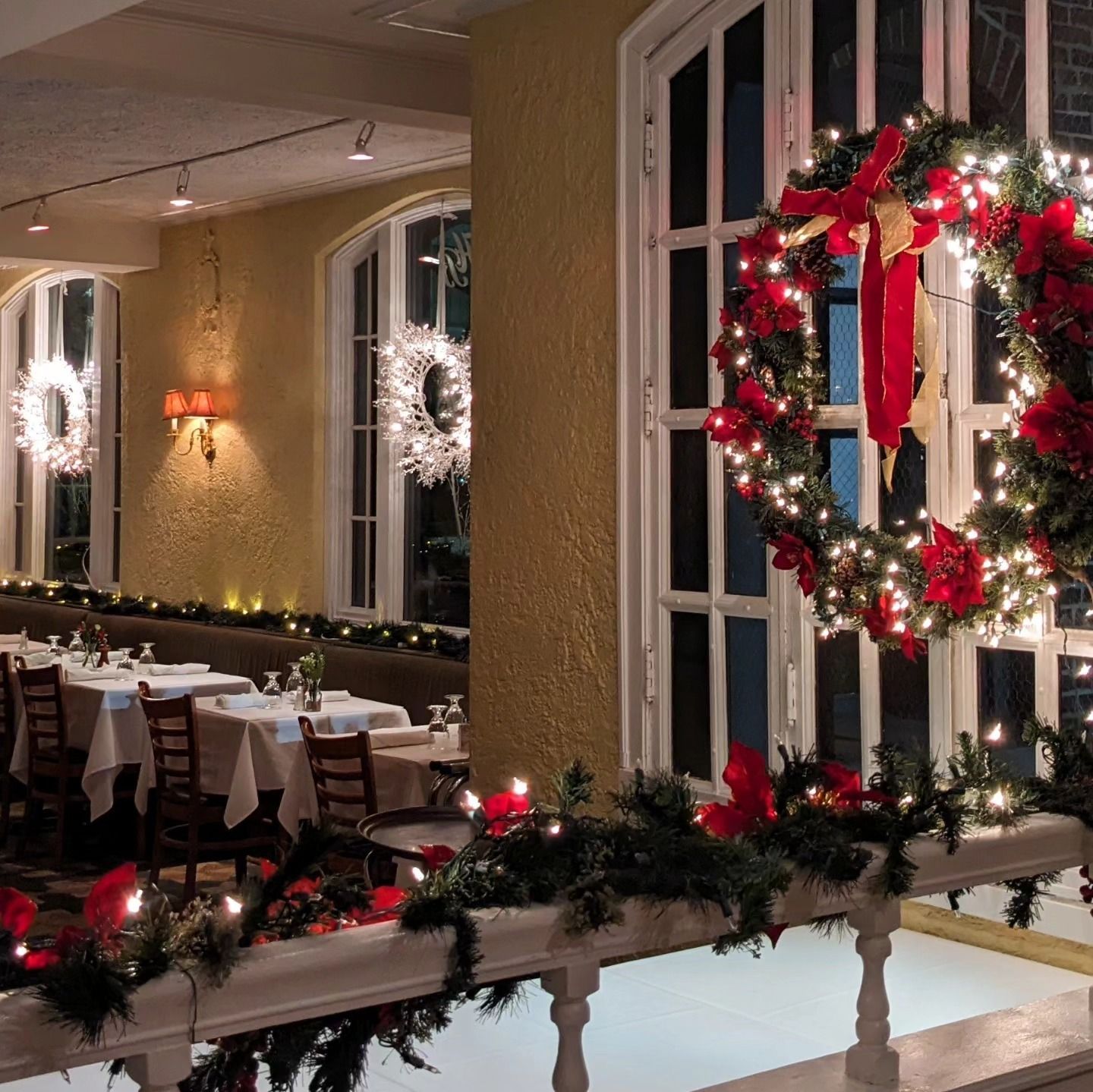 Festive restaurant balcony with lit wreaths, garland, and white-clothed tables at night