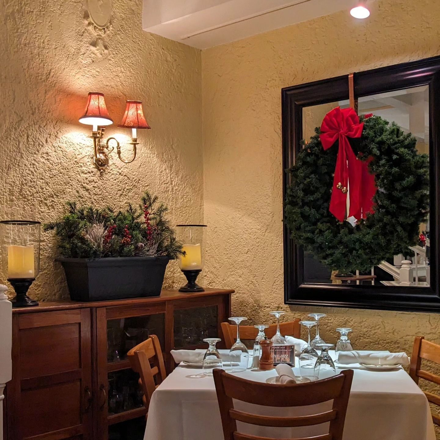 Holiday-decorated restaurant dining room with wreath, red bow, table set for dining, and warm wall sconces
