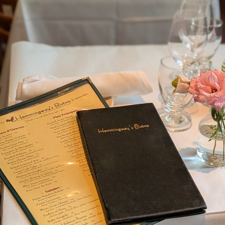 Restaurant table with menu, black billfold, folded napkin, and pink flowers in glass vases