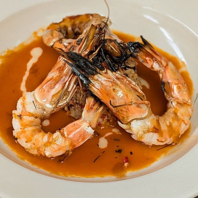 Plated shrimp in orange sauce, topped with charred garnish on a white dish