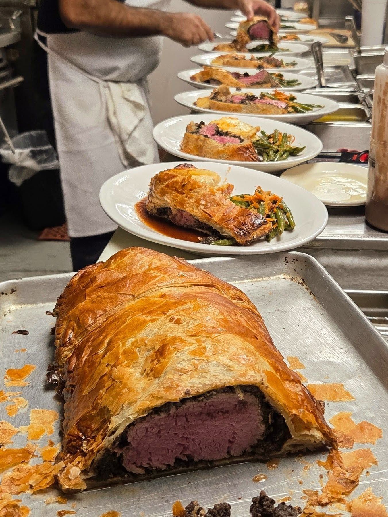 Sliced beef Wellington plated on a stainless steel kitchen counter, with more servings being prepared behind it