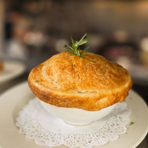 Golden pot pie in a white bowl on a plate with a lace doily, topped with rosemary