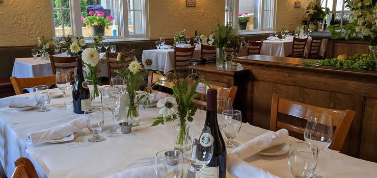 Elegant restaurant dining room with white tablecloths, wine bottles, and floral centerpieces
