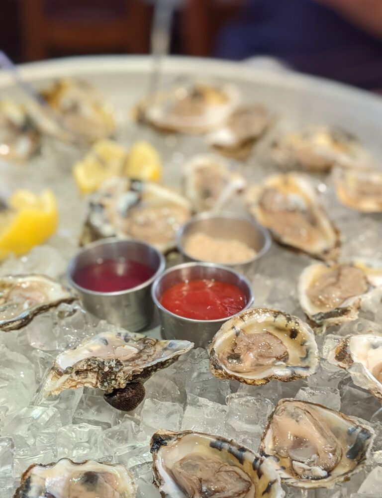 Plate of raw oysters on ice with lemon wedges and two red sauce cups