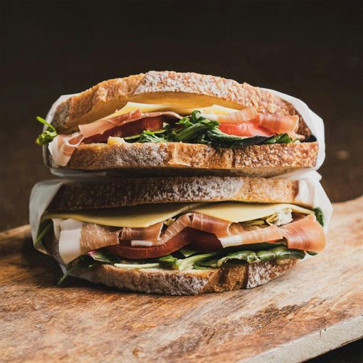 Stacked sandwich with ham, lettuce, and tomato on a wooden board