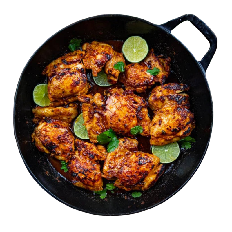 Overhead view of spiced chicken pieces in a black skillet, garnished with lime slices and cilantro