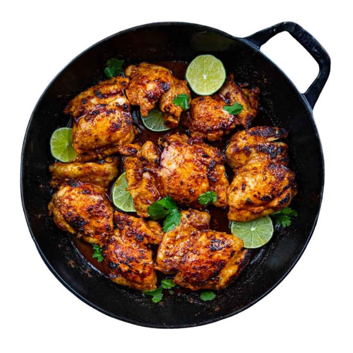 Overhead view of spiced chicken pieces in a black skillet, garnished with lime slices and cilantro